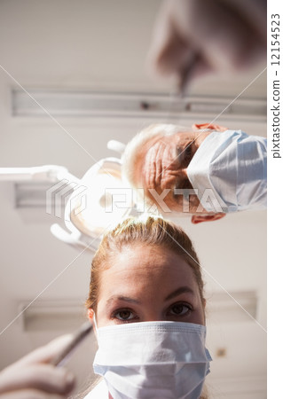 Dentist and assistant leaning over patient with tools Dentist and assistant leaning over patient with tools 12154523