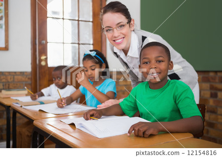 Pretty teacher helping pupil in classroom 12154816