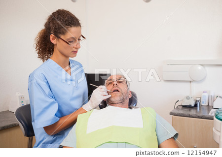 Dentist examining a patients teeth in the dentists chair 12154947