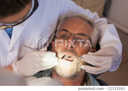 Dentist examining a patients teeth in the dentists chair 12155261