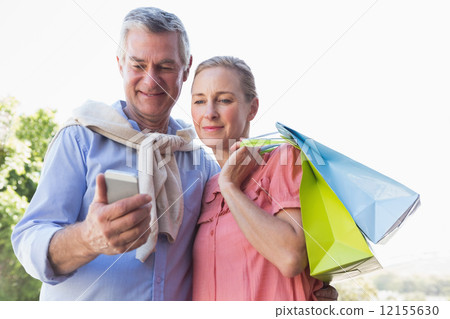 Happy senior couple looking at smartphone holding shopping bags Happy senior couple looking at smartphone holding shopping bags 12155630
