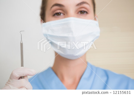 Dentist in surgical mask holding dental explorer Dentist in surgical mask holding dental explorer 12155631