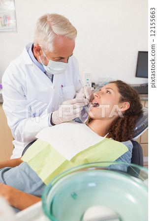 Dentist examining a patients teeth in the dentists chair 12155663