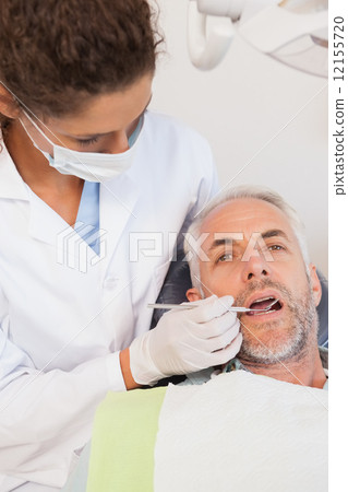 Dentist examining a patients teeth in the dentists chair 12155720