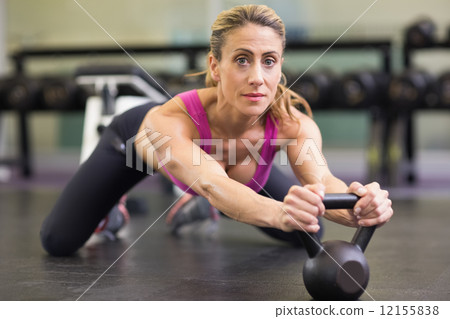Serious woman lifting kettle bell in gym Serious woman lifting kettle bell in gym 12155838