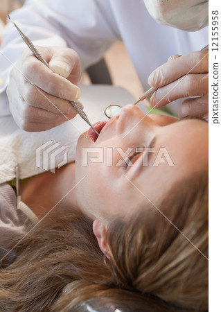 Dentist examining a patients teeth in the dentists chair 12155958