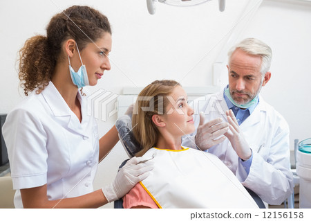 Dentist examining a patients teeth in the dentists chair with as 12156158