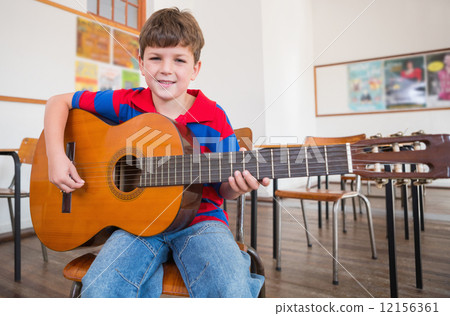 Cute pupil playing guitar in classroom