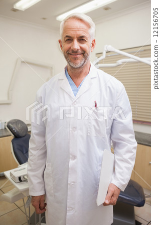 Dentist smiling at camera beside chair 12156705