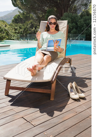 Stock Photo: Woman reading book on sun lounger by pool