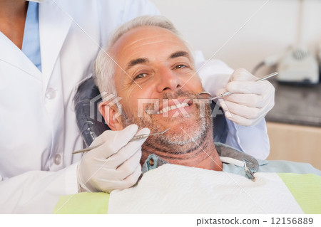 Dentist examining a patients teeth in the dentists chair 12156889
