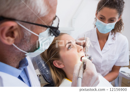 Dentist examining a patients teeth in the dentists chair with as 12156900