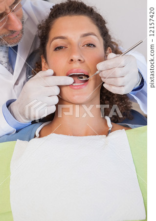 Dentist examining a patients teeth in the dentists chair 12157420