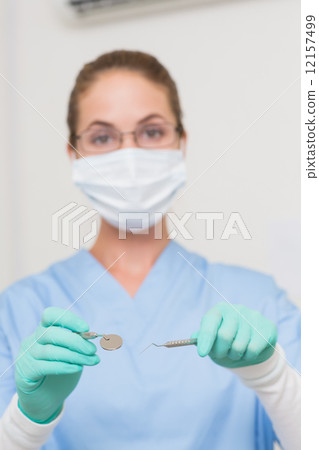 Dentist in blue scrubs holding tools looking at camera Dentist in blue scrubs holding tools looking at camera 12157499