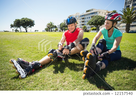 Fit mature couple tying up their roller blades on the grass Fit mature couple tying up their roller blades on the grass 12157540