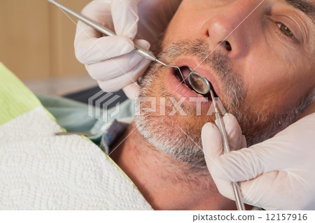 Dentist examining a patients teeth in the dentists chair 12157916