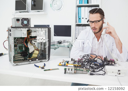 Computer engineer looking at broken device and making a phone ca Computer engineer looking at broken device and making a phone ca 12158092