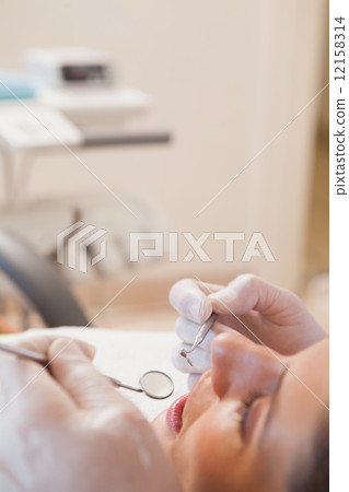 Dentist examining a patients teeth in the dentists chair 12158314