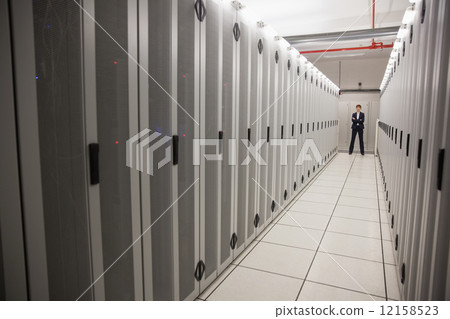 Serious technician standing in server hallway Serious technician standing in server hallway 12158523