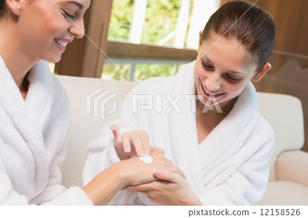 Woman applying cream to friend's hand Woman applying cream to friend's hand 12158526