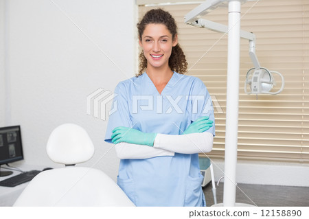 Dentist in blue scrubs smiling at camera beside chair Dentist in blue scrubs smiling at camera beside chair 12158890