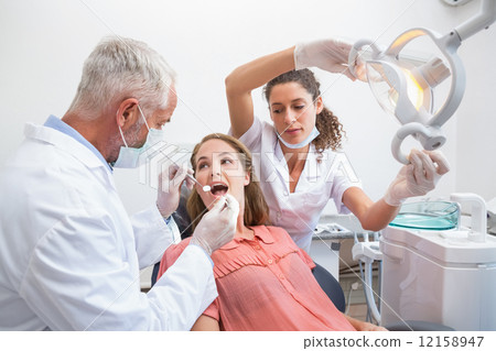 Dentist examining a patients teeth in the dentists chair with as 12158947