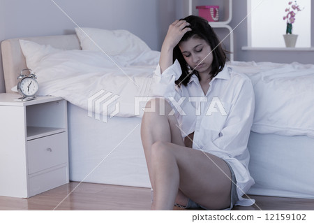 Sad brunette sitting on floor beside her bed Sad brunette sitting on floor beside her bed 12159102