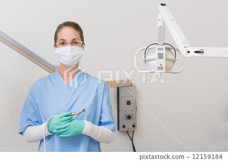 Dentist in blue scrubs holding dental drill looking at camera 12159184