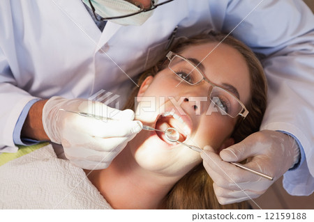 Dentist examining a patients teeth in the dentists chair under b Dentist examining a patients teeth in the dentists chair under b 12159188