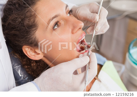 Dentist examining a patients teeth in the dentists chair 12159216