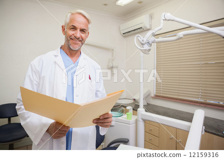 Dentist smiling at camera holding folder 12159316