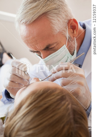 Dentist examining a patients teeth in the dentists chair 12159337