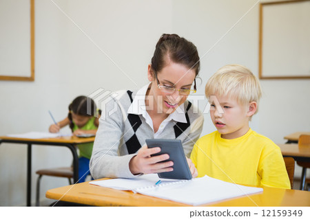 Pretty teacher helping pupil in classroom Pretty teacher helping pupil in classroom 12159349