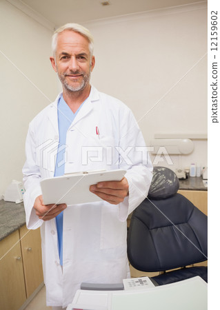 Dentist smiling at camera holding clipboard 12159602