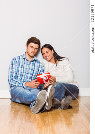 Young couple sitting on floor with gift 12159971