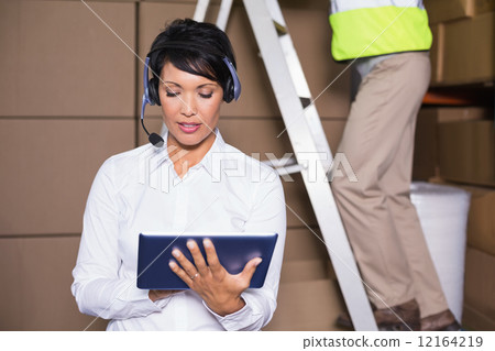 Pretty warehouse manager using tablet during busy period 12164219