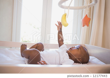 Adorable baby boy lying in his crib playing with mobile Adorable baby boy lying in his crib playing with mobile 12177443