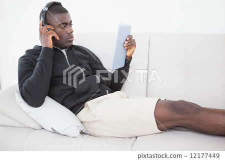 Casual man sitting on his sofa listening to music on tablet pc 12177449