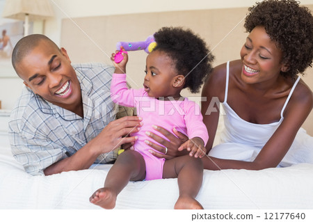 Happy parents playing with baby girl on bed together 12177640
