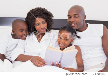 Happy family reading book together in bed 12178402