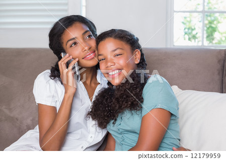 Happy mother and daughter using smartphone together on sofa Happy mother and daughter using smartphone together on sofa 12179959