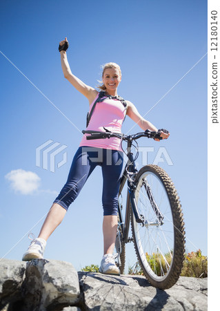 Fit pretty cyclist on a rocky terrain smiling at camera Fit pretty cyclist on a rocky terrain smiling at camera 12180140