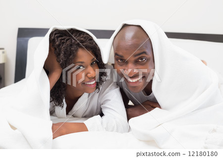 Happy couple lying on bed together under the duvet 12180180