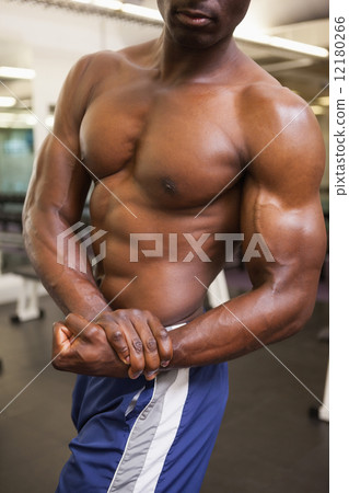 Mid section of a shirtless muscular man in gym Mid section of a shirtless muscular man in gym 12180266