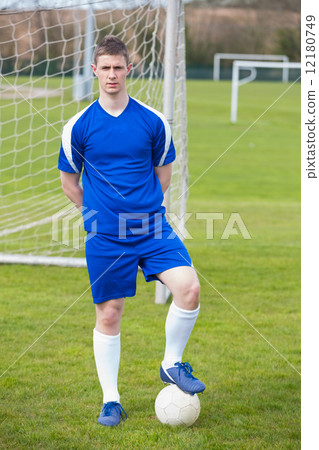 Football player in blue posing with the ball on pitch 12180749