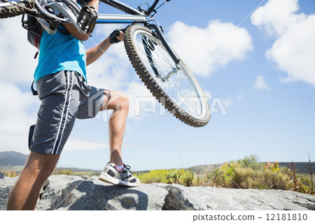 Fit man walking up rocky terrain holding mountain bike 12181810