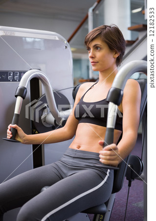 Smiling brunette using weights machine for arms 12182533