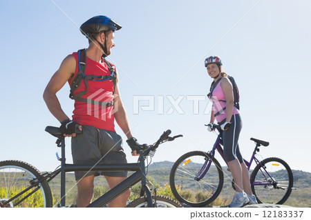 Fit cyclist couple standing at the summit smiling at each other 12183337