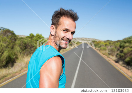 Fit man jogging on the open road smiling at camera 12183983