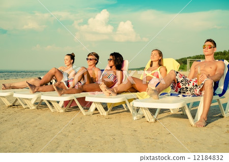 Group of multi ethnic friends sunbathing on a deck chairs on a beach Group of multi ethnic friends sunbathing on a deck chairs on a beach 12184832